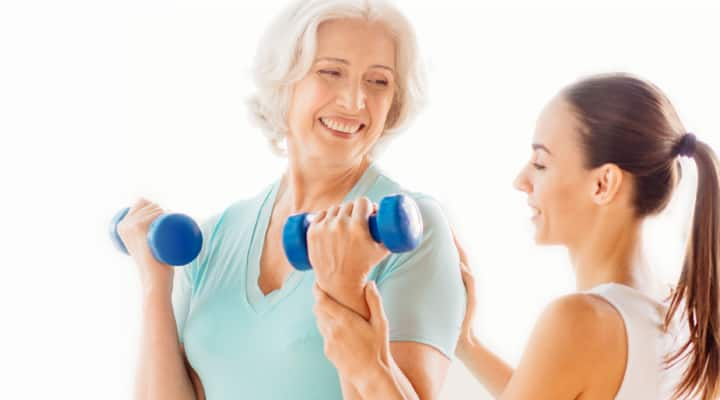 Younger woman helping older woman exercise with dumbells