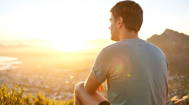 Man sitting on a cliff watching the sunset